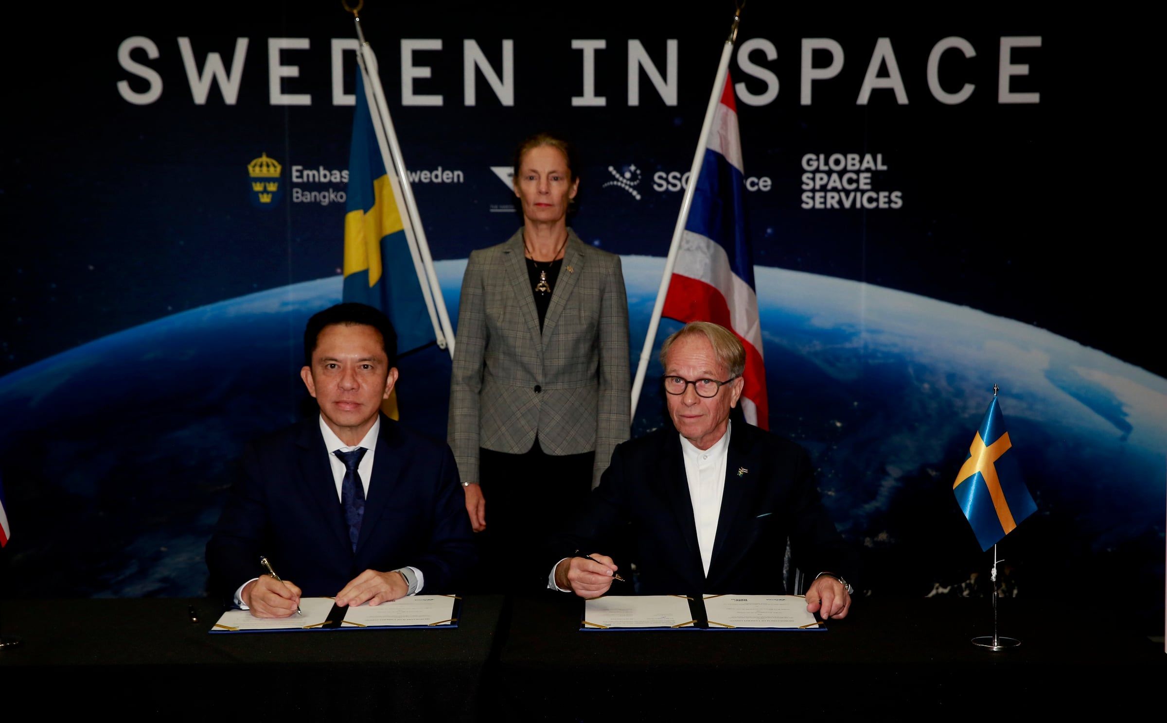 Dr. Pakorn Apaphant of GISTDA and Alf Öskog of Global Space Services sign the agreement at a table, with Ambassador Anna Hammargren standing behind them in front of a "Sweden in Space" backdrop with Swedish and Thai flags.